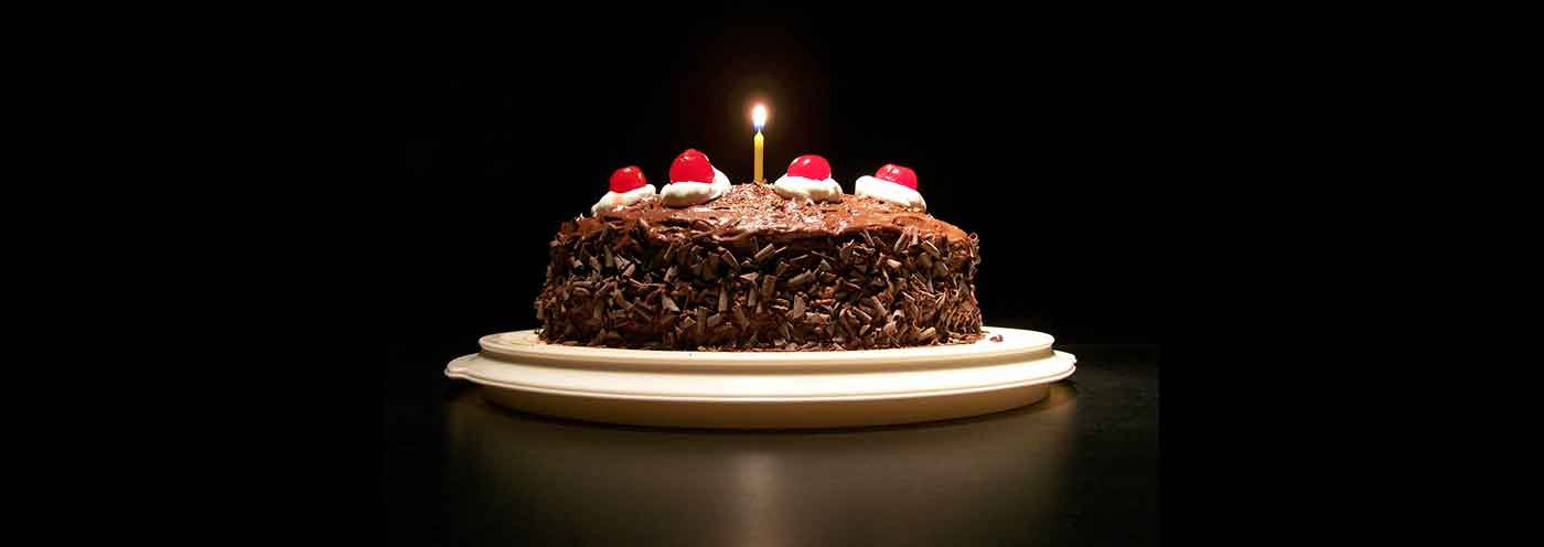 Photograph of a chocolate cake lit by a single candle