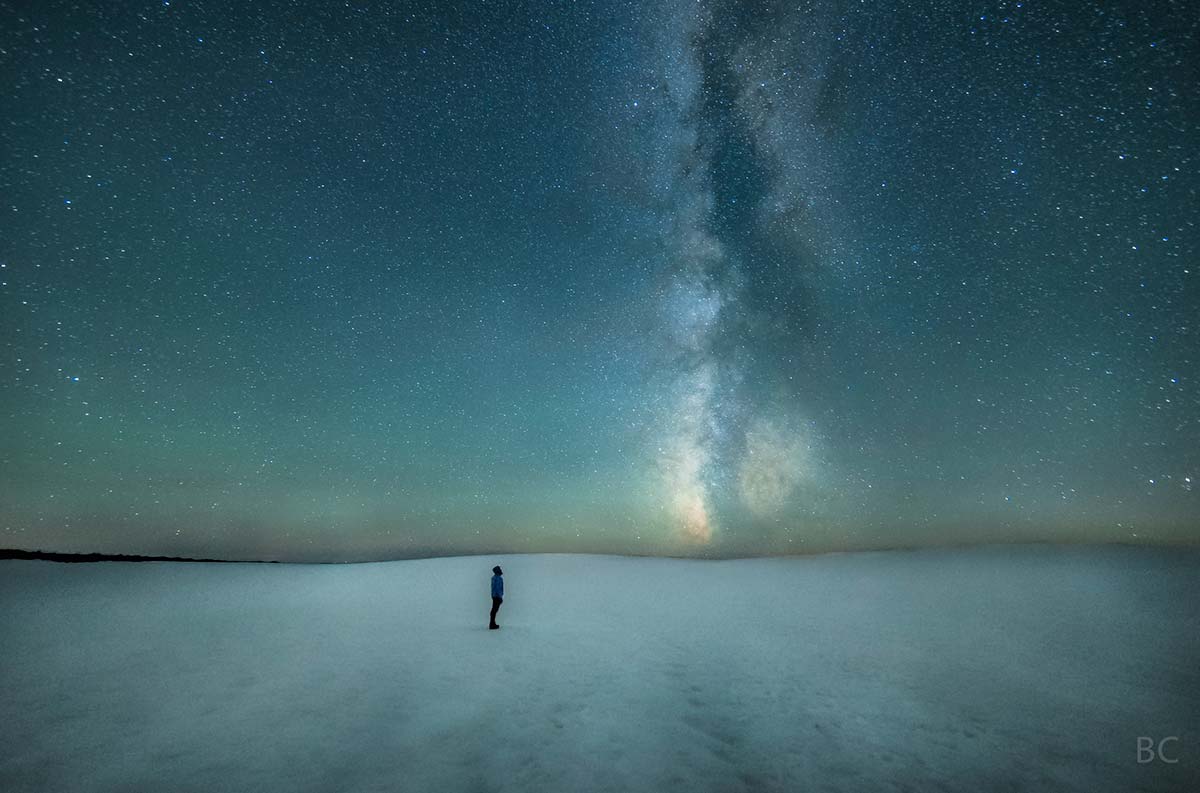 Photograph of a man standing at the summit of the South Sister volcano in Oregon, under the Milky Way